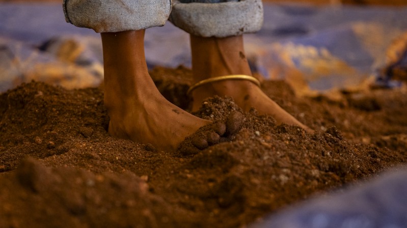 A imagem mostra os pés de uma pessoa descalça pisando na terra.