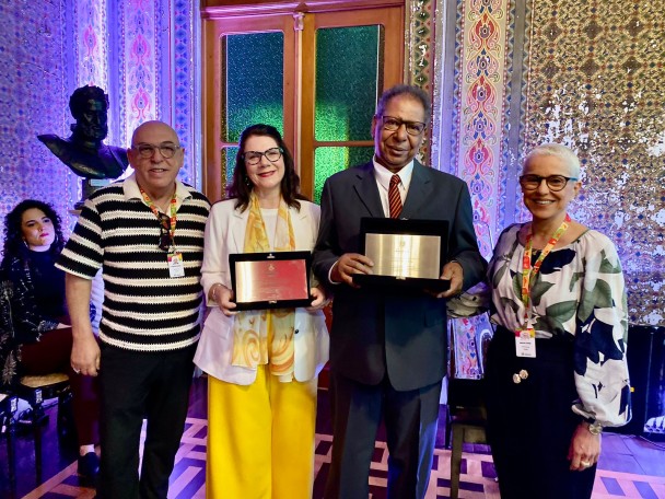 No centro da imagem, a ex-presidente do CEC, Alessandra Mota, e o presidente interino do CEC, Antônio Carlos Côrtes, exibem placas de metal. Ao lado deles, a secretária de Estado da Cultura, Beatriz Araujo, à direita, e à esquerda, o coordenador do Sistema Estadual de Cultura, Ruben Oliveira posam para a fotografia.