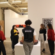 A imagem mostra um grupo de pessoas visitando uma exposição no Margs acompanhadas de um mediador. 