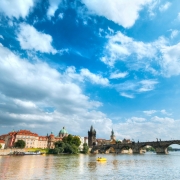 Fotografia de Praga, na República Tcheca. À frente aparece um rio e, ao fundo, uma ponte e prédios históricos