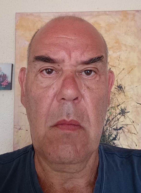 Um homem branco e calvo vestindo camiseta azul olha sério para a câmera