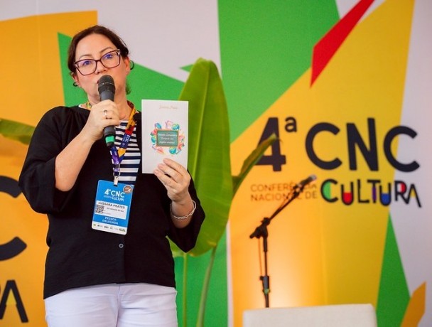 Uma mulher segura um livro sobre o palco da 4ª Conferência Nacional de Cultura