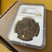 Close-up de uma moeda antiga brasileira encapsulada e certificada pela Numismatic Guaranty Company (NGC). O rótulo diz:
“1835-Dated Brazil Brass
Fonrobert-8872 Piratini
Silvered
AU Details
Tooled
20907429-003”.
A moeda tem a inscrição “REPUBLICA RIOGRANDENSE” com uma balança, raios de sol e a data de 1835 em destaque. A peça está acondicionada em um estojo plástico sobre uma superfície de papelão.

