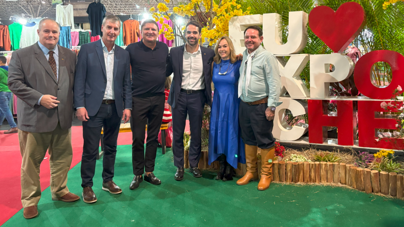 Seis pessoas posam sorridentes em frente ao letreiro da Expotchê. Entre os presentes, estão o secretário de Estado da Cultura, Eduardo Loureiro, o governador do Estado, Eduardo Leite, e o secretário de Turismo, Ronaldo Santini.