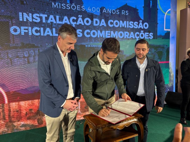 Governador assina um documento acompanhado do vice-governador Gabriel Souza e do Secretário de Estado da Cultura.