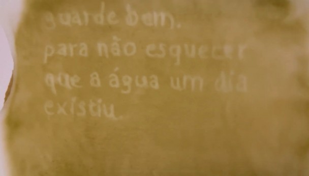 Imagem de uma superfície em tom amarelado com uma escrita em branco que diz: "guarde bem, para não esquecer que a água um dia existiu."