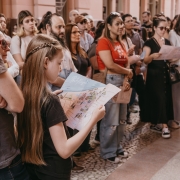 Menina de cabelos longos e trançados segura e observa um mapa ilustrado de Porto Alegre, cercada por outras pessoas que também participam de uma atividade cultural.