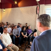 Visto de trás do palco, a imagem mostra o público prestando atenção a fala do Secretário Eduardo Loureiro. 