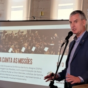 Imagem mostra Secretário Eduardo Loureiro, homem branco, de cabelos curtos e grisalhos, usando terno azul escuro e camisa azul mais claro. Atrás dele aparece uma tela de projeção.