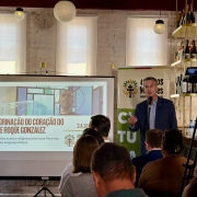 Imagem mostra Secretário da Cultura, Eduardo Loureiro falando de pé em microfone diante de uma plateia sentada. Atrás dele, aparece uma tela de apresentação. 