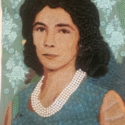 Retrato artístico confeccionado com diferentes materiais têxteis e objetos aplicados sobre uma superfície verde-água. A imagem mostra uma mulher de cabelos escuros, representados por tecidos trançados e franzidos, usando um colar de várias voltas de pérolas e uma veste rendada em tom azul-esverdeado. O rosto é construído com milhares de pequenos grãos em tons de bege e marrom, formando delicadamente os contornos e detalhes da expressão. Ao redor da figura há bordados florais claros, botões e pequenas contas verdes espalhadas pela composição, enriquecendo a textura da obra.