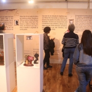 A imagem mostra uma parte da exposi&ccedil;&atilde;o &ldquo;Mem&oacute;ria Cantada: Wilson Ney&rdquo;. A sala tem as paredes escritas com a traj&eacute;toria do artista e algumas pessoas circulam pelo local. 