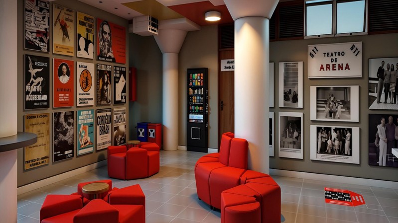 A imagem mostra o interior de um espa&ccedil;o cultural, com paredes decoradas por cartazes e fotografias relacionadas ao teatro. &Agrave; esquerda, h&aacute; uma grande composi&ccedil;&atilde;o de p&ocirc;steres de diferentes espet&aacute;culos, em preto e branco e coloridos. No centro, aparecem poltronas e pufes vermelhos, dispostos em uma &aacute;rea de conviv&ecirc;ncia, al&eacute;m de uma m&aacute;quina de bebidas. &Agrave; direita, a parede re&uacute;ne fotografias emolduradas de apresenta&ccedil;&otilde;es e o letreiro &ldquo;Teatro de Arena&rdquo;. O ambiente tem piso claro, colunas brancas, ilumina&ccedil;&atilde;o quente e decora&ccedil;&atilde;o inspirada na hist&oacute;ria do teatro.