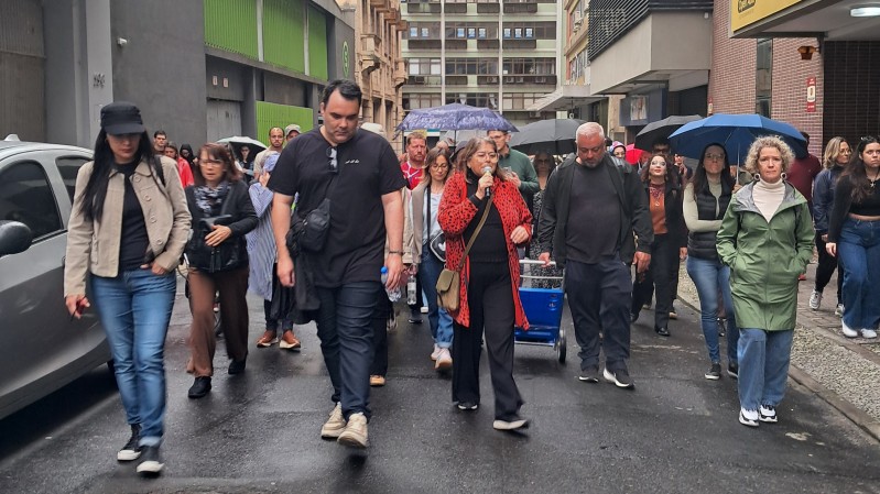 Um grupo de pessoas realiza uma caminhada pelas ruas do Centro Hist&oacute;rico de Porto Alegre. &Agrave; frente do grupo, uma guia fala ao microfone