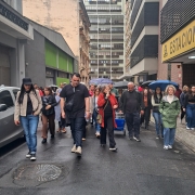 Um grupo de pessoas realiza uma caminhada pelas ruas do Centro Hist&oacute;rico de Porto Alegre. &Agrave; frente do grupo, uma guia fala ao microfone