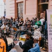 A foto mostra uma roda de samba. H&aacute; muitas pessoas na foto, dan&ccedil;ando e tocando instrumentos. Em primeiro plano, aparece um cartaz de divulga&ccedil;&atilde;o da evento com a frase "Viva a casa de todas as culturas".